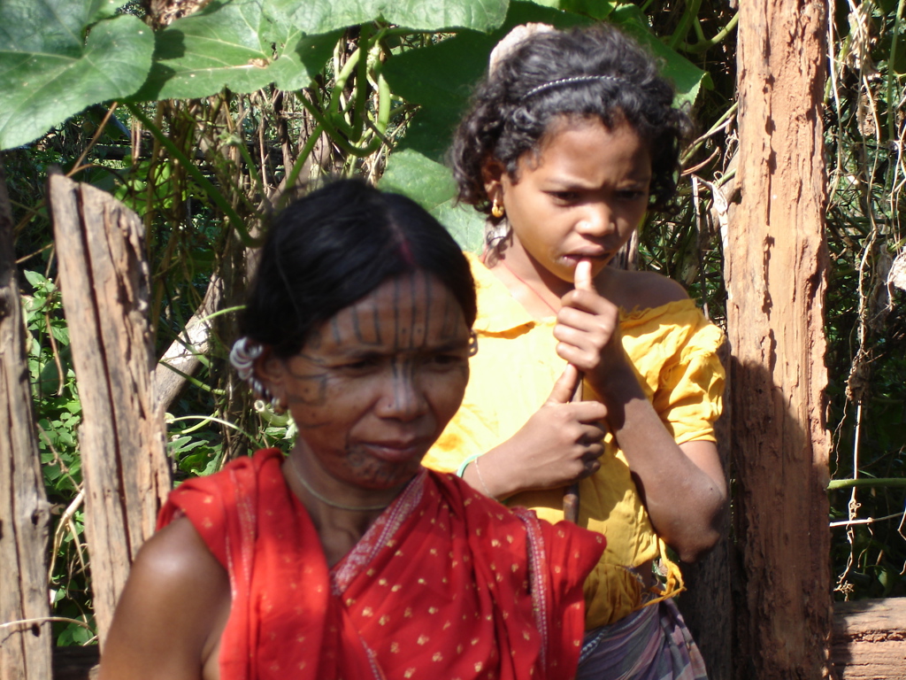 Portret van twee vrouwen in Orissa, India, in traditionele kleding bij een houten hek.