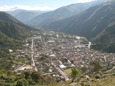 Uitzicht over Baños in Ecuador, gelegen in een groene bergvallei met rivier en brug.