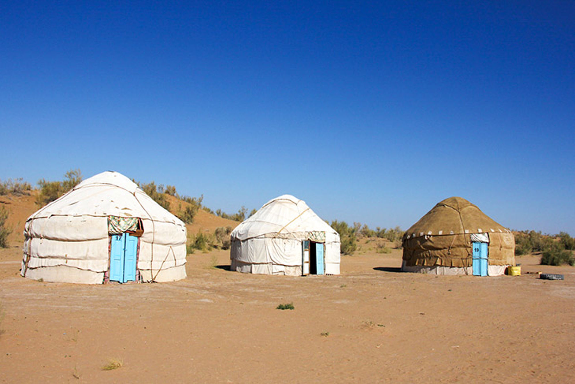 Overnachten in yurts in Oezbekistan Drie traditionele yurts in een woestijnlandschap onder een strakblauwe lucht.