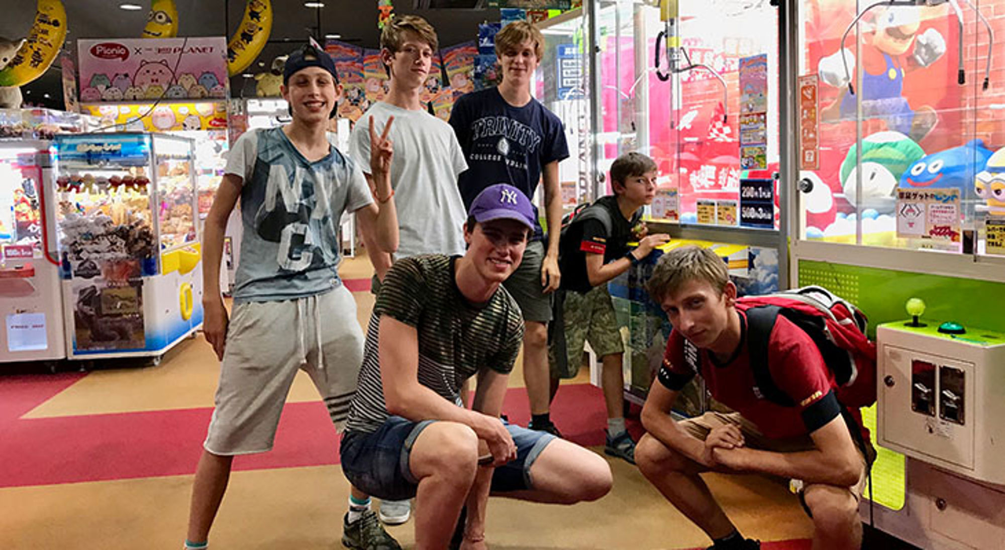 Jongens poseren in een Japanse arcadehal tussen grijpmachines en kleurrijke gameposters.