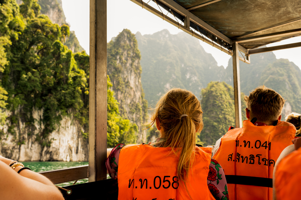Jongeren maken een boottocht in Thailand langs groene kalksteenkliffen en helder water.
