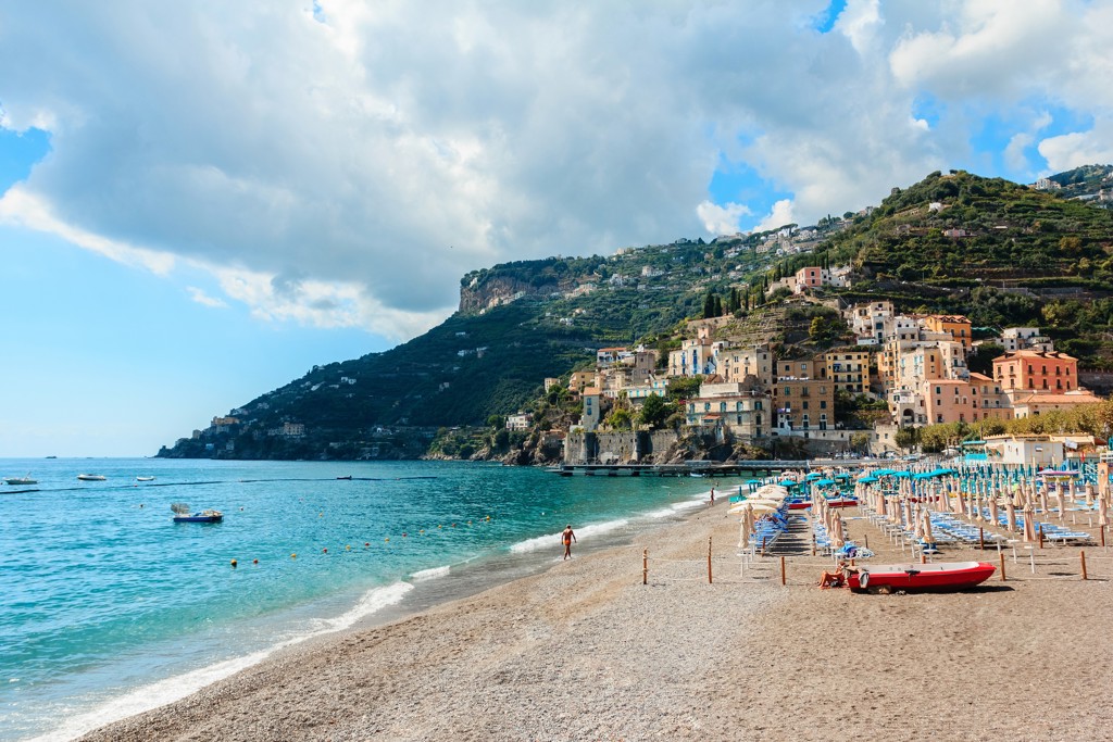 Strand en kustplaats aan de Amalfikust in Zuid-Italië, met kleurrijke huizen tegen de groene heuvels.