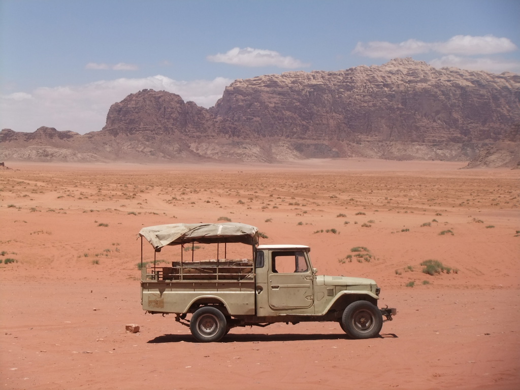 Safari-jeep in de Wadi Rum-woestijn in Jordanië, met rode zandvlakte en rotsbergen op de achtergrond.