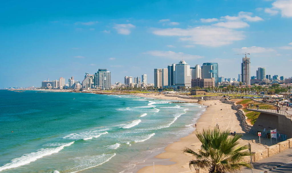 Skyline van Tel Aviv aan de Middellandse Zee met zandstrand en golven onder een blauwe lucht.