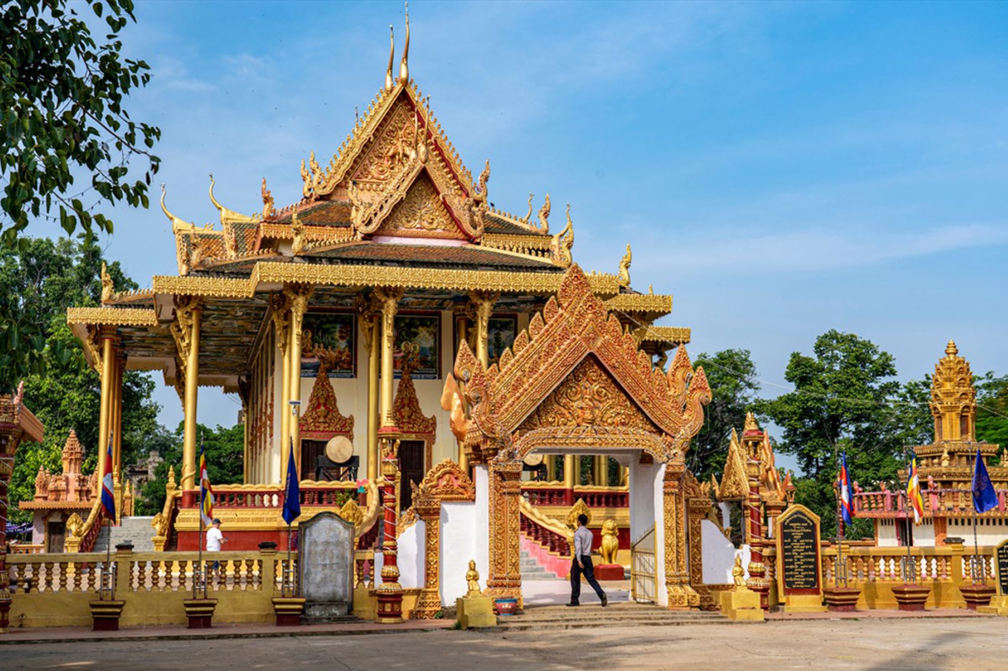 Gouden tempelcomplex in Cambodja met sierlijke poort en traditionele Khmer-architectuur onder blauwe lucht.