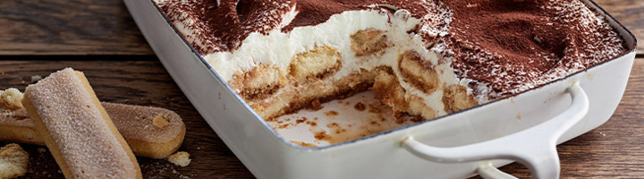 Tiramisu in ovenschaal met laag mascarpone en cacao, met een stuk eruit geschept.