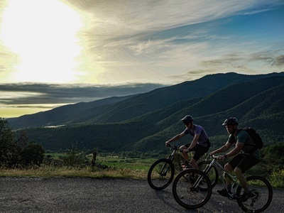 Twee mountainbikers op Route Canigou met uitzicht op de Pyreneeën bij zonsondergang.