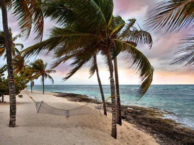 Hangmat tussen palmbomen op een strand aan zee in Cuba bij zonsondergang.
