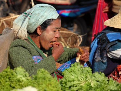 Vrouw met traditionele hoofddoek eet op een markt in Myanmar tijdens de 25-daagse Birma-route.