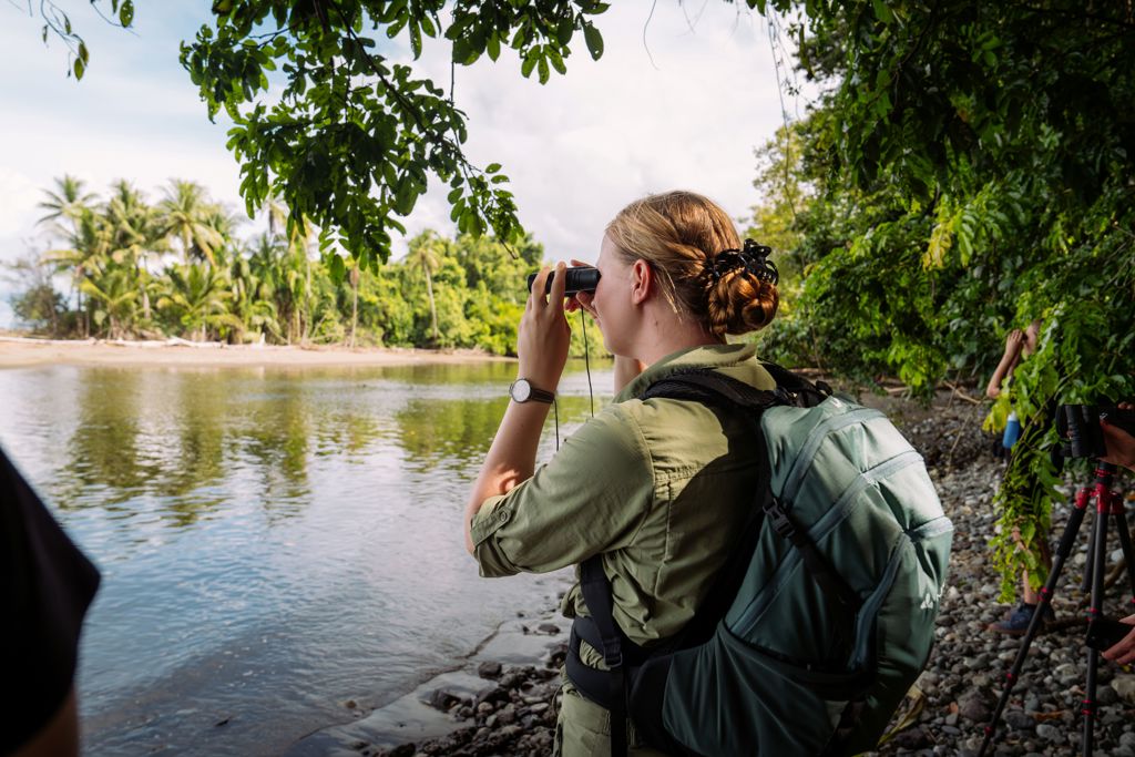 22-35ers reis Costa Rica: reiziger spot wildlife met verrekijker langs een rivier in het regenwoud.