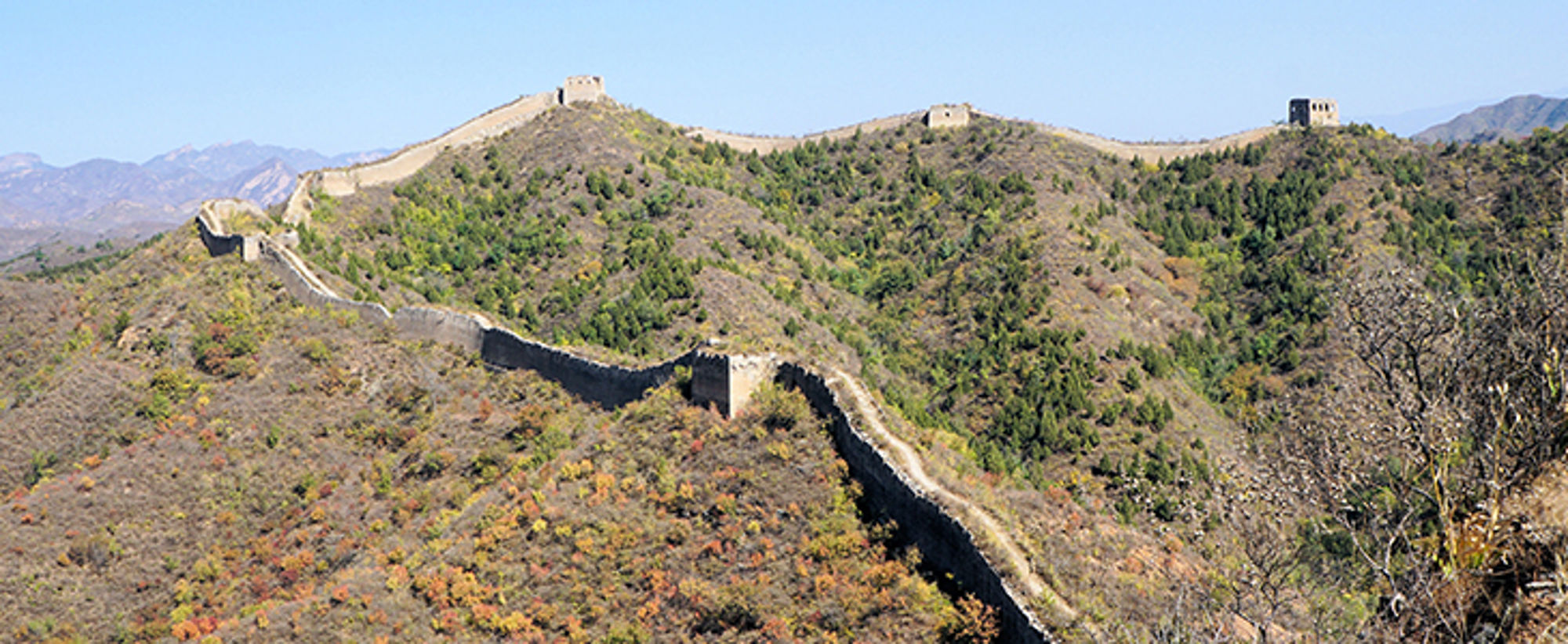 De Chinese Muur slingert over groene heuvels onder een heldere blauwe lucht.