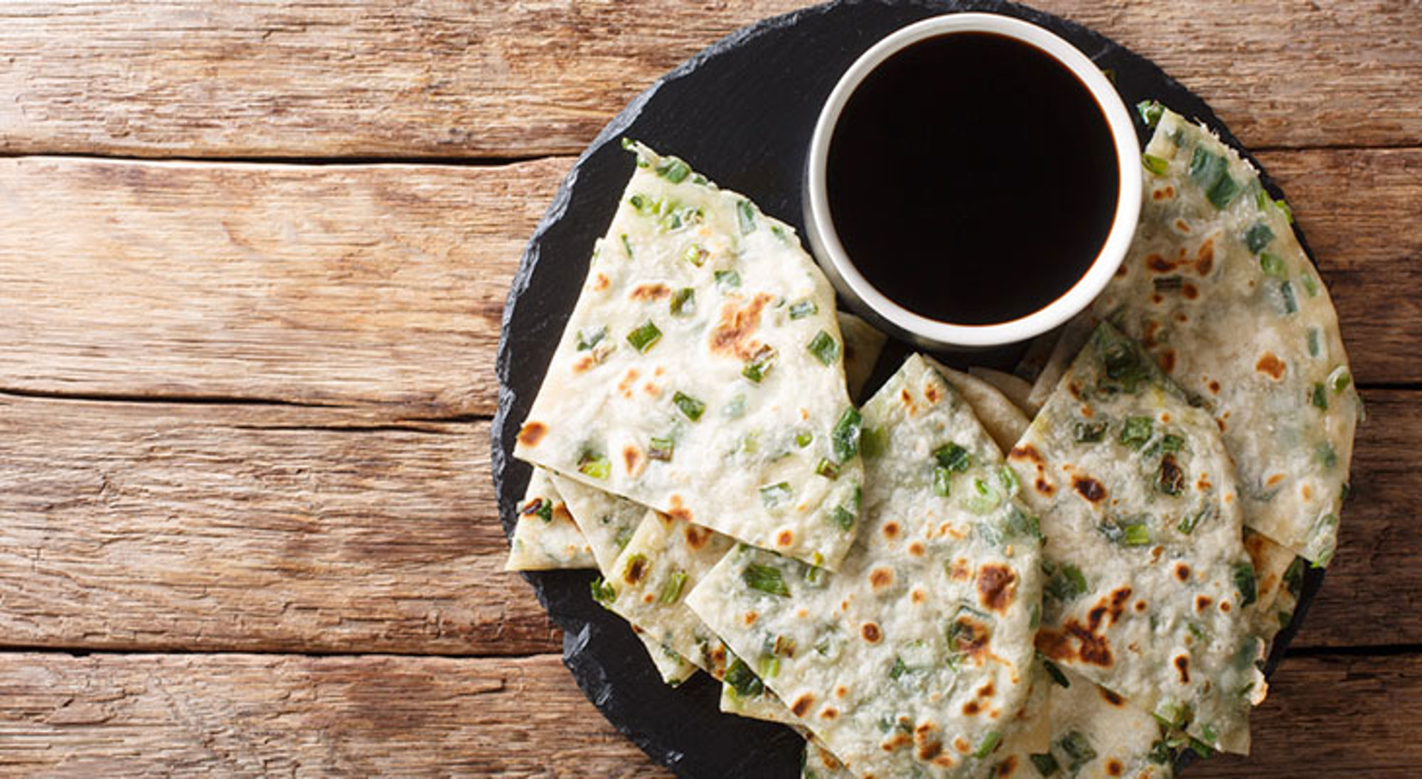 Vegetarisch Chinees gerecht Bord met knapperige pannenkoekjes met lente-ui en een kommetje sojasaus op een houten tafel.
