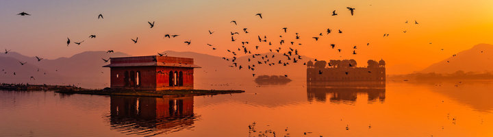 Zonsondergang boven Jal Mahal in Jaipur, met vogels boven het meer en weerspiegeling in het water.