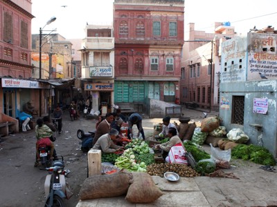 Groentemarkt in een straat in Noord-India, met verkopers en stapels verse groenten voor traditionele gevels.