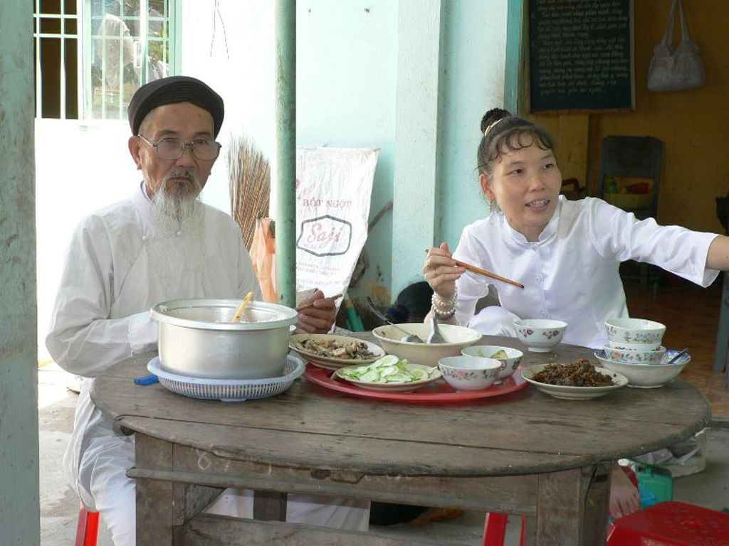 Lokale maaltijd in Vietnam: man en vrouw in traditionele kleding eten aan tafel met Vietnamese gerechten.