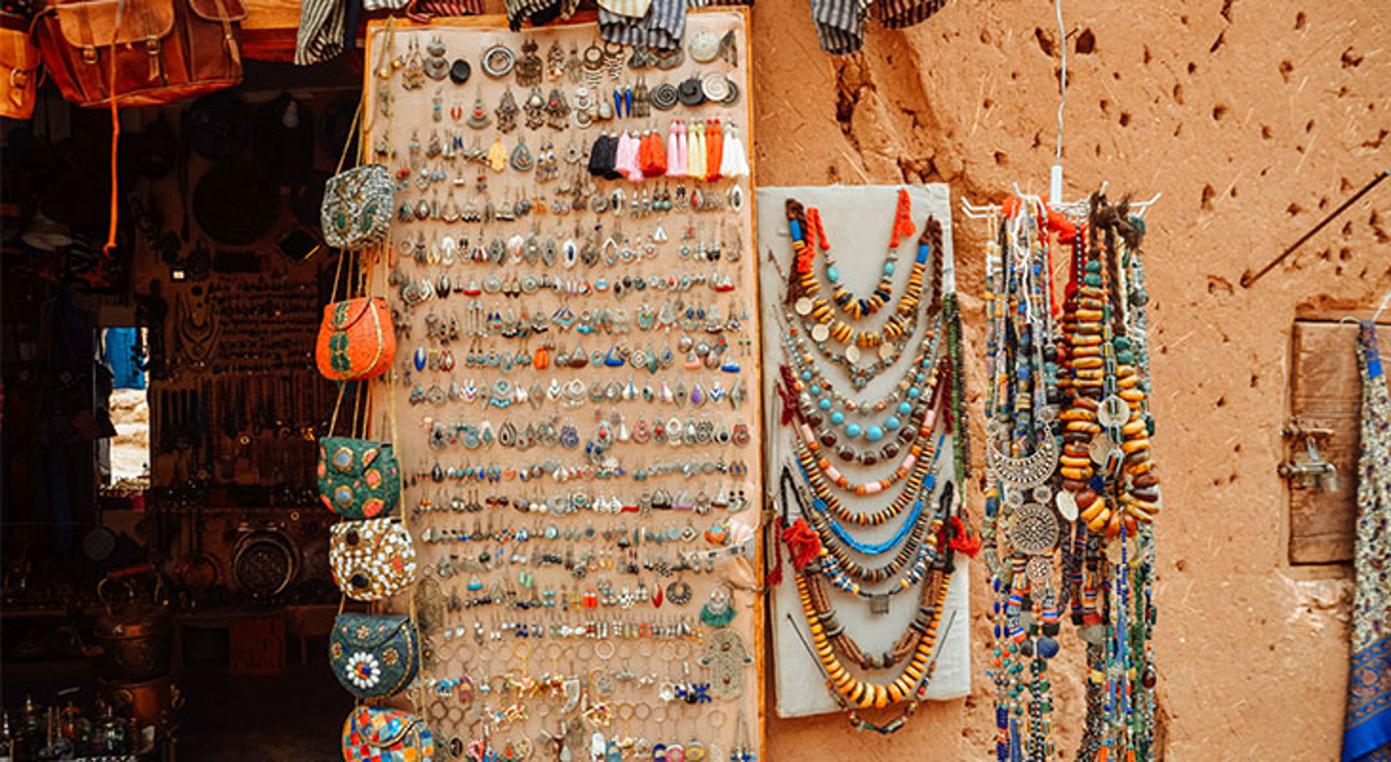 Boetiekje in Aït-Ben-Haddou Kraampje met kleurrijke sieraden en handgemaakte accessoires aan een lemen muur op een lokale markt.