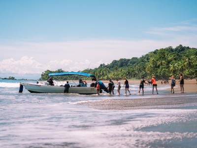 Reizigers stappen vanaf het strand in een boot aan de kust van Costa Rica, met palmbomen op de achtergrond.