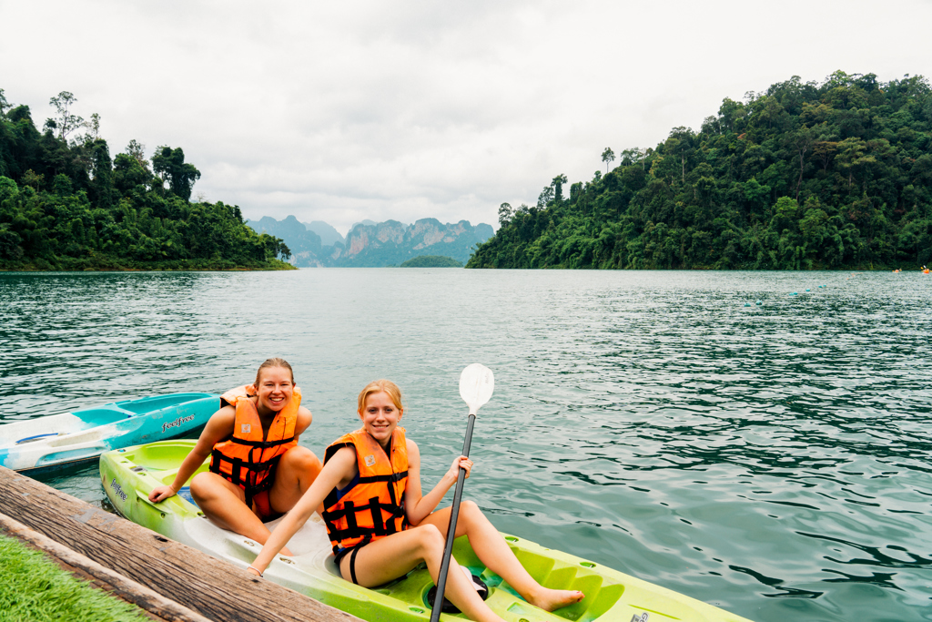 Twee reizigers kajakken op een meer in Thailand, met groene jungleheuvels op de achtergrond.