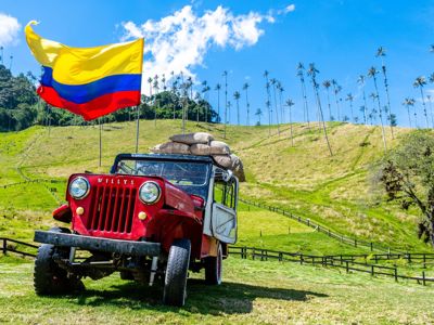 Willys-jeep met Colombiaanse vlag in de Cocora-vallei, met hoge waxpalmen en groene heuvels.