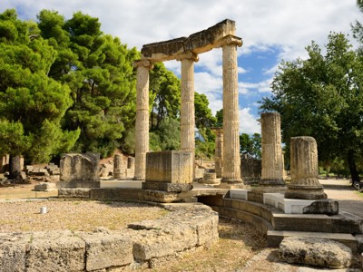 Ruïnes van de Tempel van Zeus in Olympia, Griekenland, tussen groene pijnbomen.