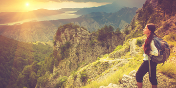 Wandelaar met rugzak op bergpad met uitzicht op berglandschap en meer in Montenegro bij zonsondergang.