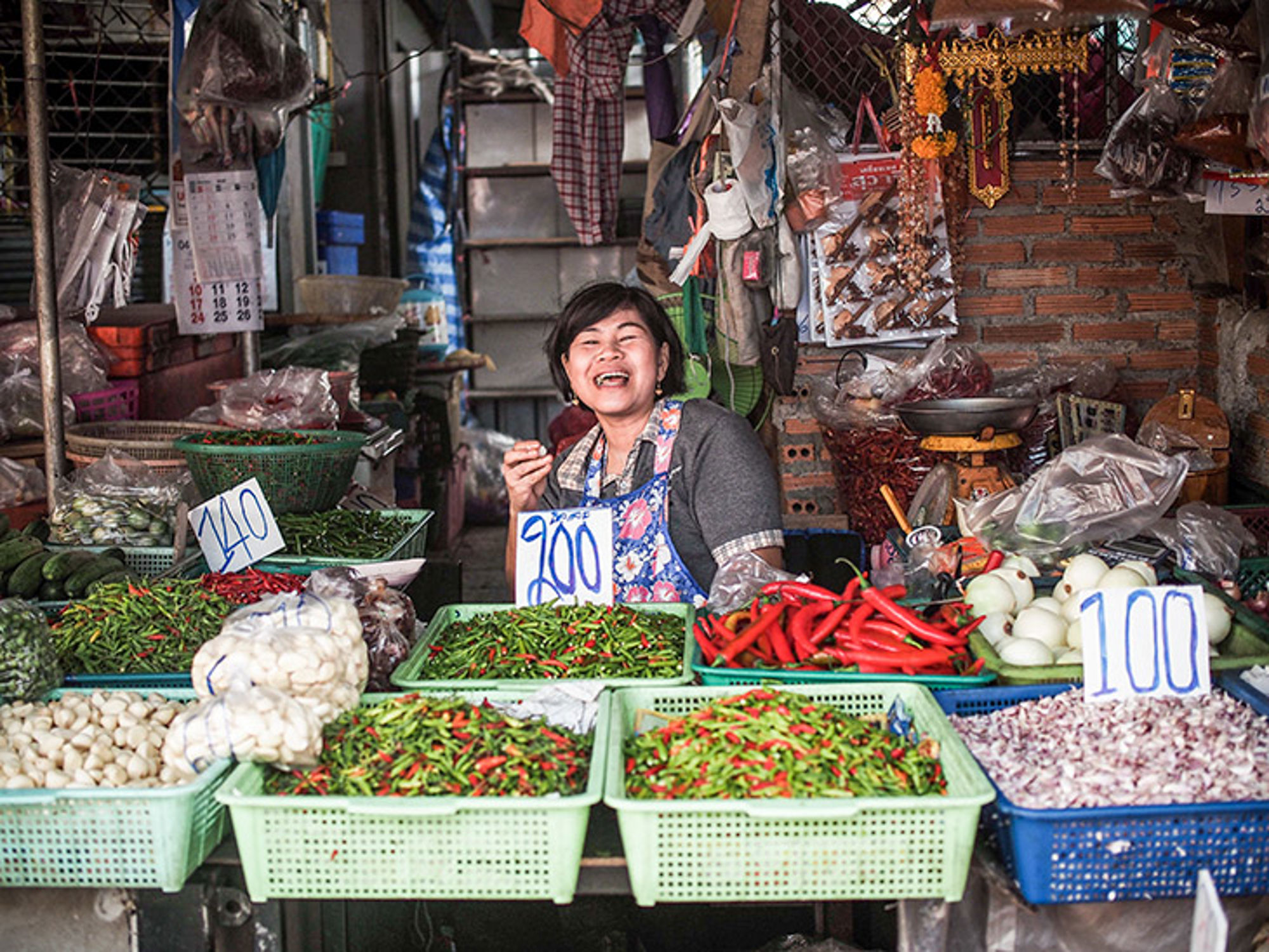 Lokale kruiden en eten in Bangkok, Thailand Lachende marktvrouw bij kraam met rode en groene pepers, uien en knoflook op een lokale markt.