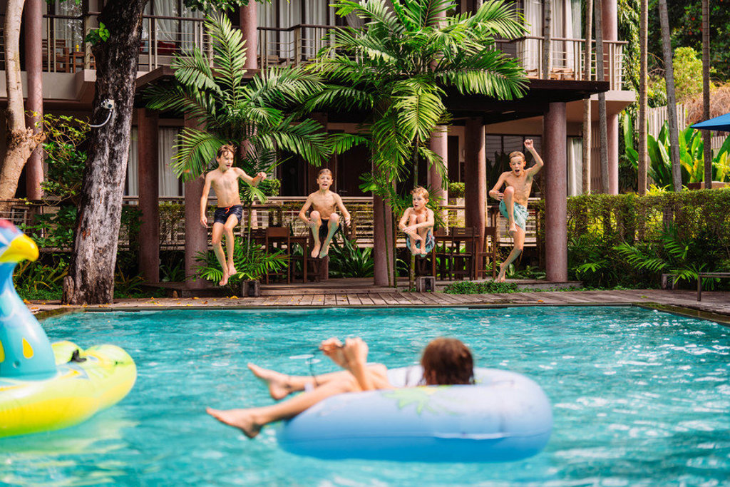 Kinderen springen in het zwembad bij een tropisch resort tijdens een familiereis Thailand.