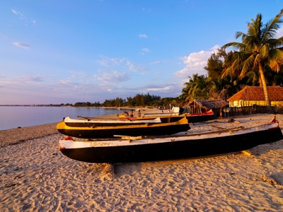 Traditionele vissersboten op het strand van Madagascar bij zonsondergang, met palmbomen en hutten op de achtergrond.