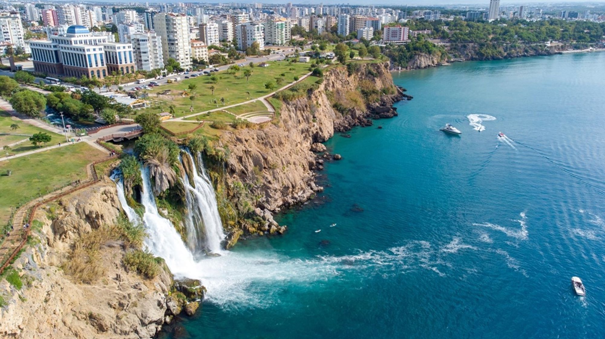 Düden-watervallen storten in de Middellandse Zee bij Antalya, met kliffen, park en skyline op de achtergrond.