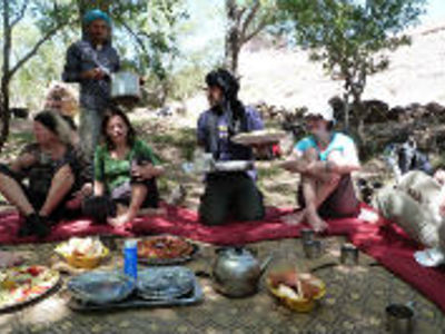 Picknicklunch tijdens de 13-daagse route door Marokko, zittend op kleden in de schaduw van bomen.