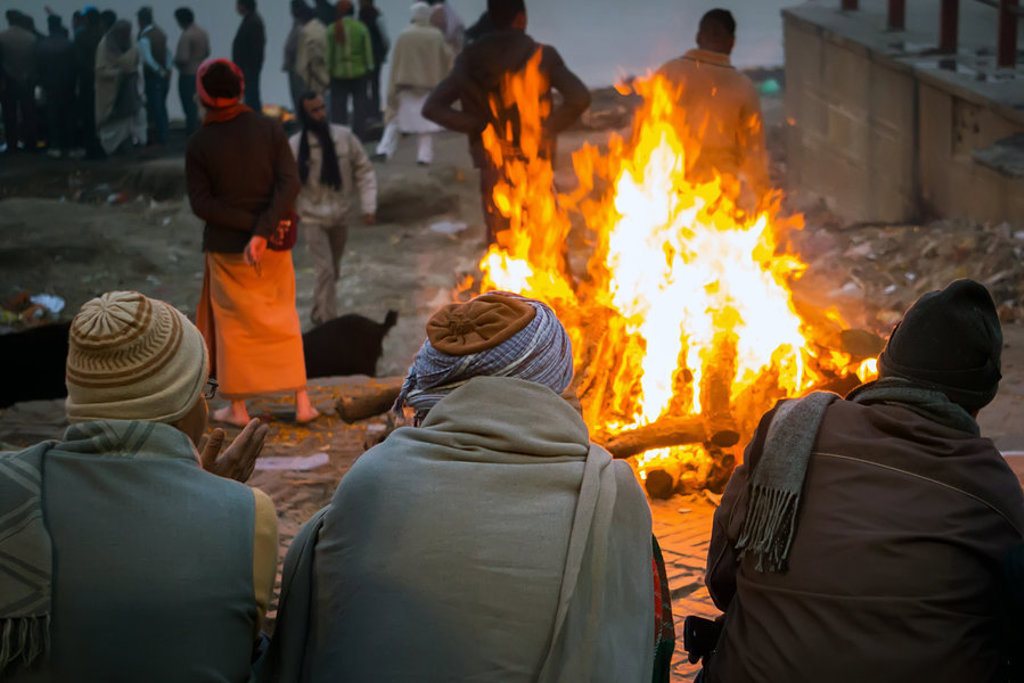 Reizigers warmen zich bij een vuur aan de oever van de Ganges in India tijdens een 22-35ers groepsrondreis.