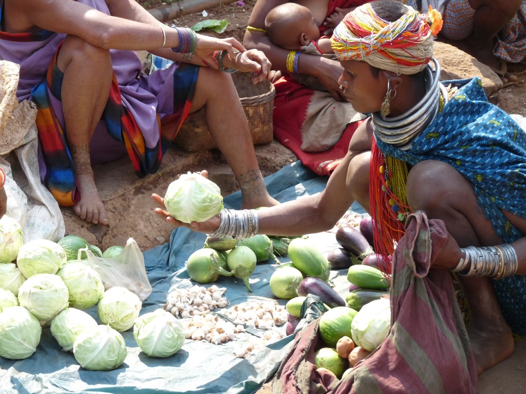 Markt in Orissa, India, met vrouw in kleurrijke sieraden die een kool verkoopt tussen verse groenten.