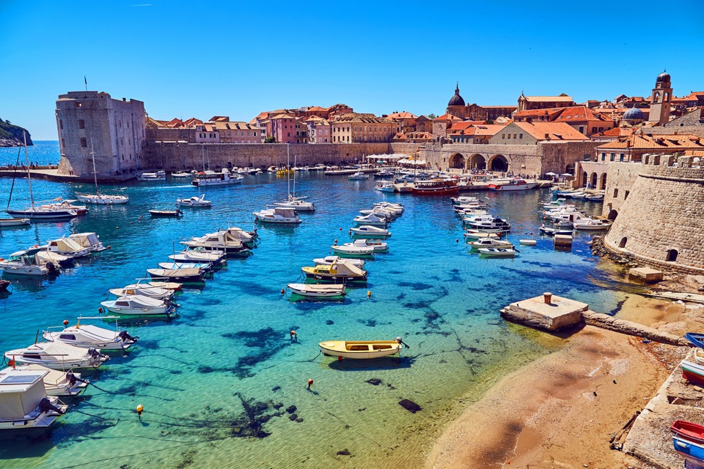 Haven van Dubrovnik met oude stadsmuren, rode daken en boten in helderblauw water.