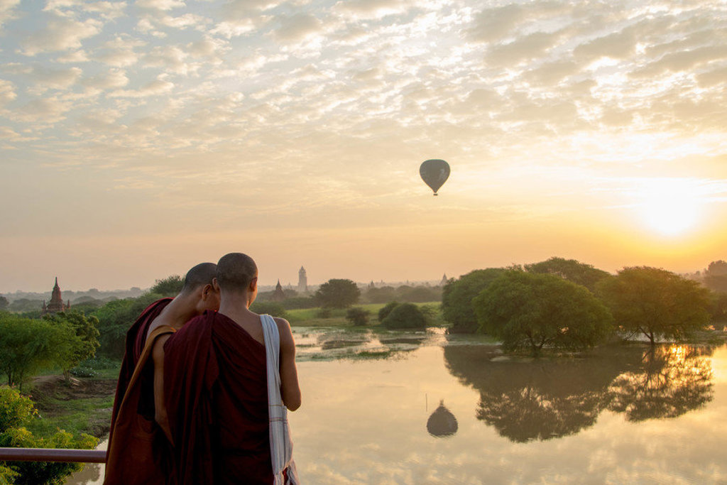 Monniken kijken uit over Bagan bij zonsopkomst, met een luchtballon boven het landschap in Myanmar.