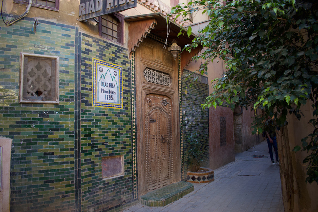 Ingang van Riad Hiba met groene mozaïektegels en houten deur in een smalle straat in Marokko.