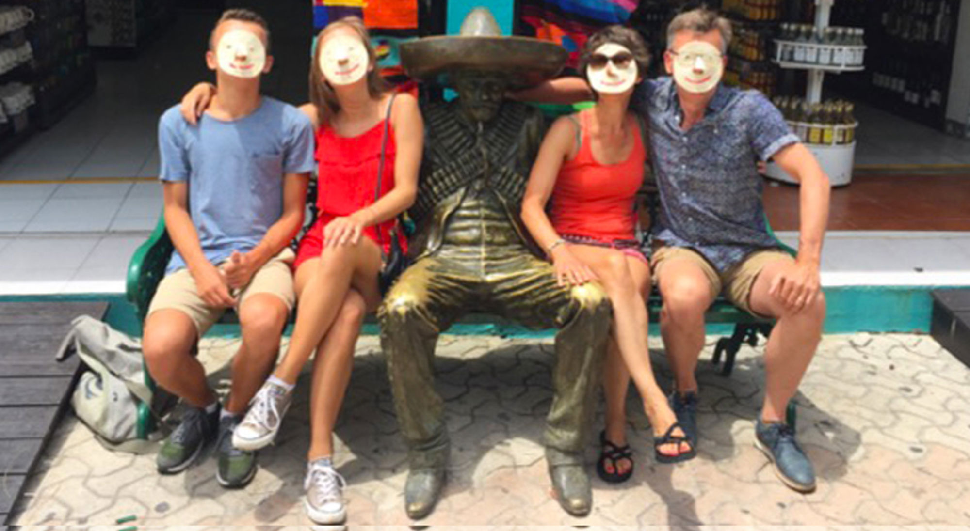Vier toeristen poseren op een bank naast een bronzen beeld met sombrero.