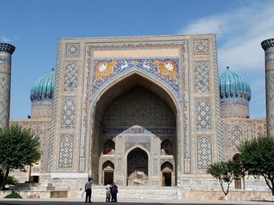 Registan-plein in Samarkand met kleurrijke madrassa, turquoise koepels en minaretten onder blauwe lucht.
