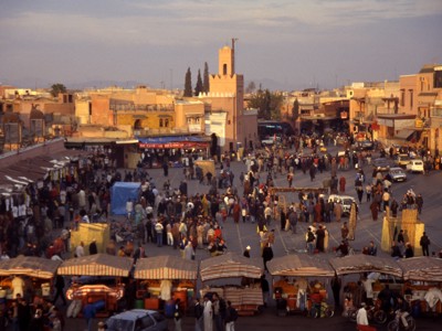 Drukke markt op het Djemaa el Fna-plein in Marrakech met kraampjes en minaret bij zonsondergang.