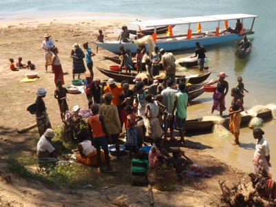 Drukke oever in Madagascar met vissersboten, mensen en visnetten bij het water.