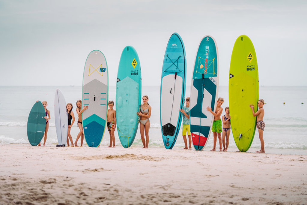 Kinderen met surf- en SUP-boards op het strand tijdens een familiereis Thailand Hoogtepunten.