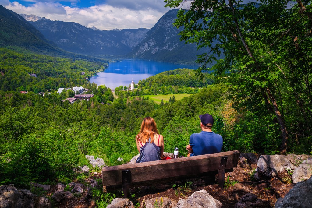 Twee reizigers op een bankje met uitzicht op het Bohinjmeer en de Julische Alpen in Slovenië.