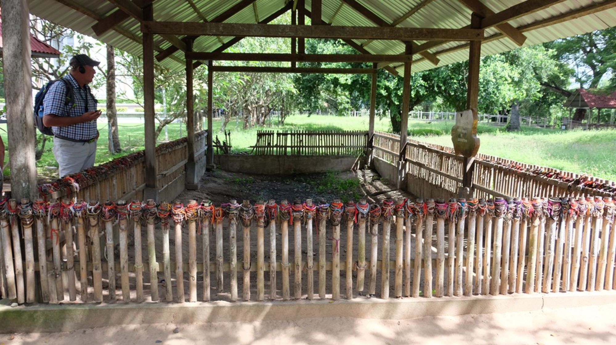 Bezoeker bij de Killing Fields van Choeung Ek in Cambodja, met gedenkplek achter een bamboehek.