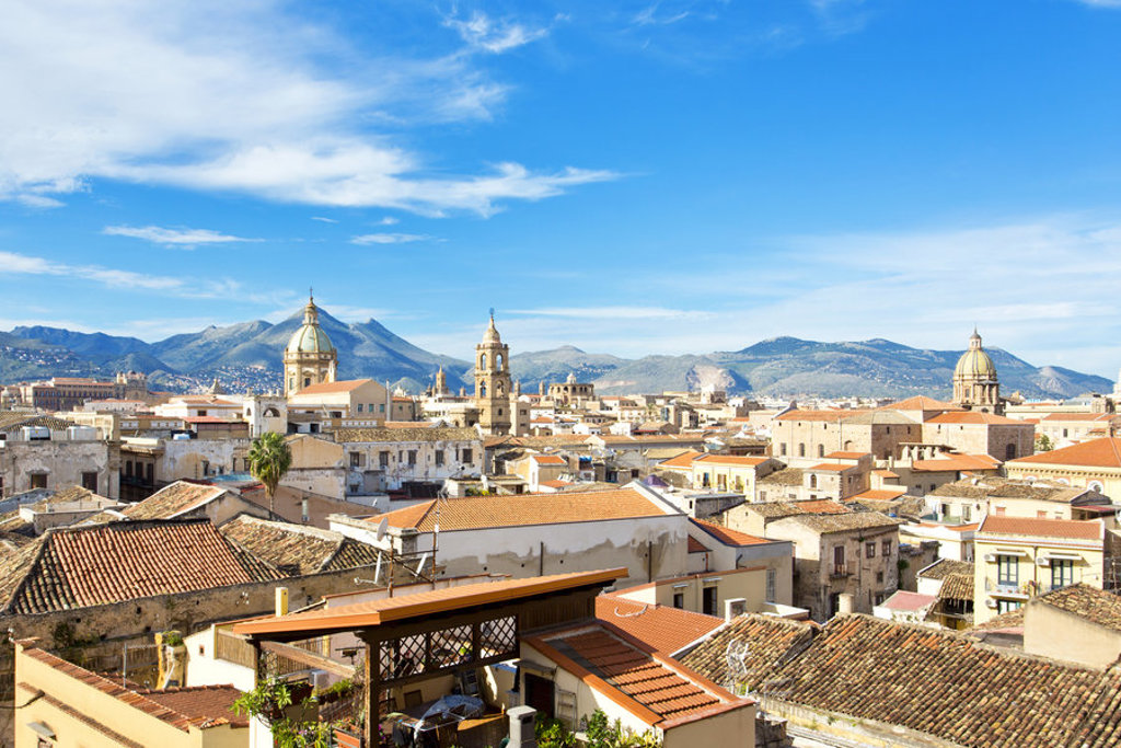 Panorama van Palermo op Sicilië met historische koepels, terracotta daken en bergen onder een blauwe lucht.