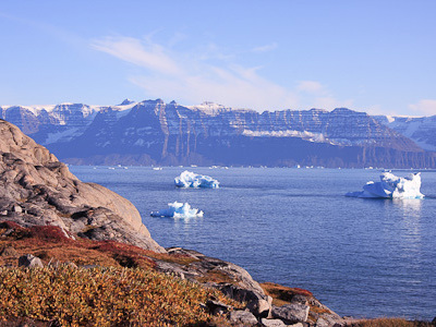 IJsbergen in een Groenlandse fjord met rotsachtige kust en besneeuwde bergen op de achtergrond.