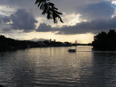 Zonsondergang boven de rivier in Maleisisch Borneo, met een bootje en palmbomen in silhouet.