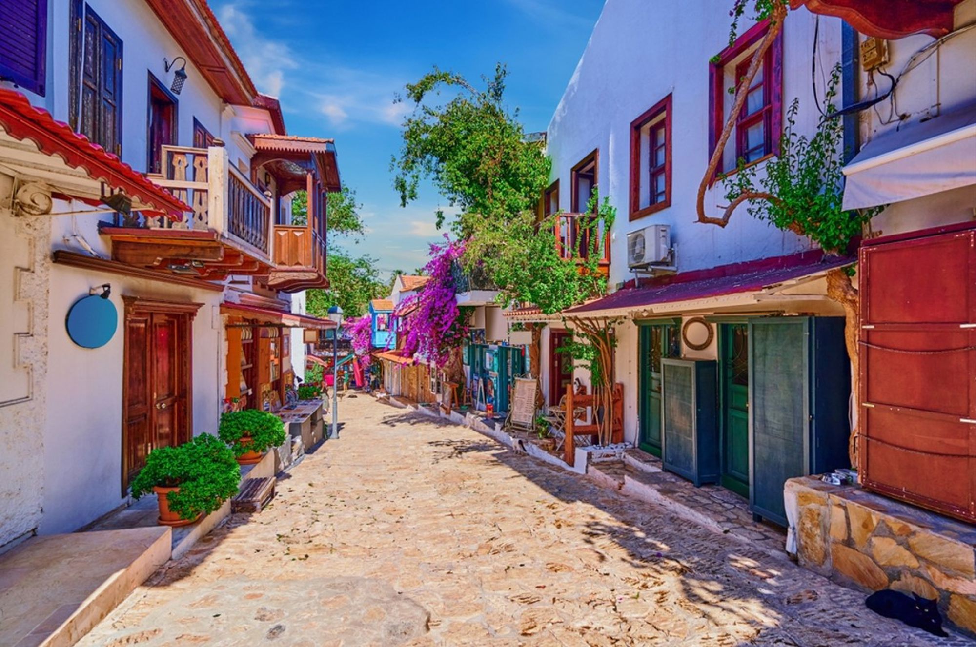 Sfeervol straatje met witte huizen, houten balkons en paarse bougainville in Turkije.