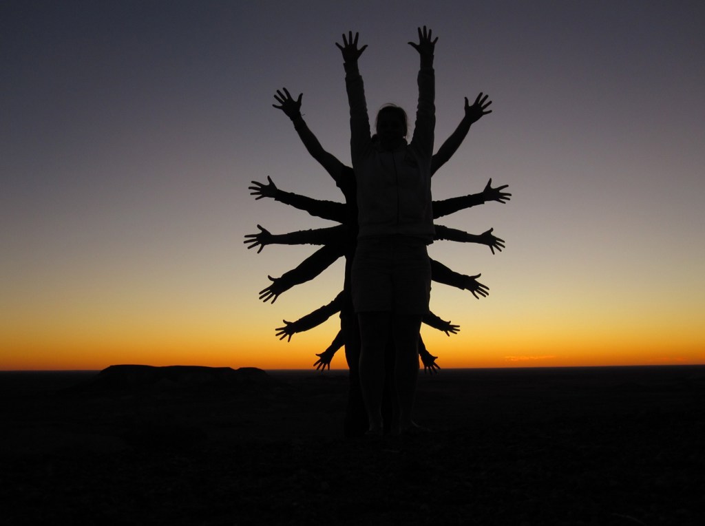 Silhouet van reizigers met uitgespreide armen bij zonsondergang in de Australische outback tijdens groepsrondreis Australië.