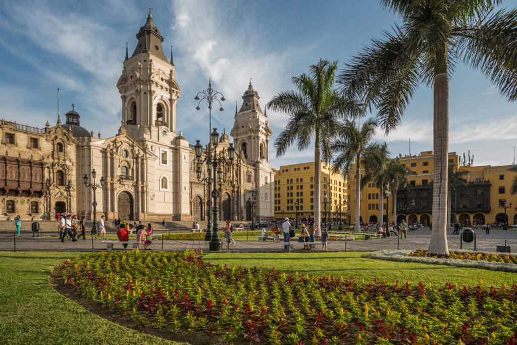 Kathedraal aan Plaza Mayor in Lima, Peru, met palmbomen en bezoekers in de zon.
