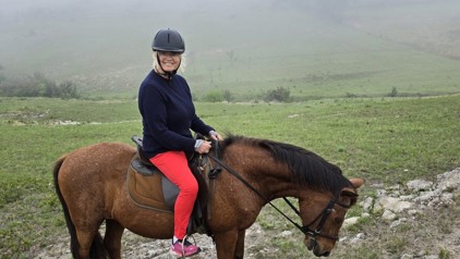 Ruiter op paard tijdens een groepsrondreis door Zuid-Afrika, met groen heuvellandschap op de achtergrond.