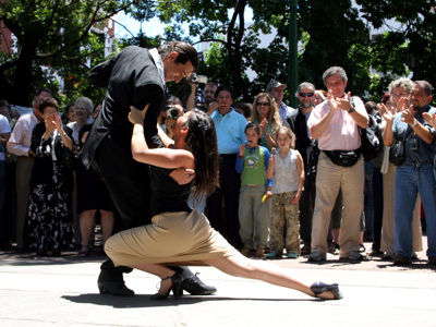 Tango-optreden in Buenos Aires met danspaar en toeschouwers op een zonnig plein.